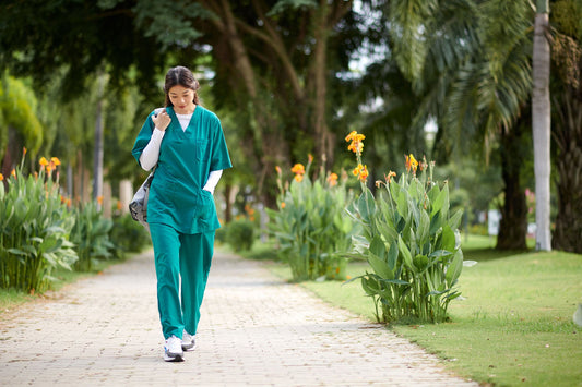 Nurse in green medical scrubs walking to work along a tree-lined park path